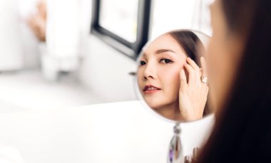 Gülümseyen, güzel, güzel Asyalı kadın güzellik bembeyaz giysiler içinde temiz, sağlıklı beyaz ten. Düşen ve eğlenen kız Home.Asia güzellik salonundaki aynaya bak.