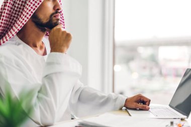 Laptop bilgisayar izleme teknolojisine bakan yakışıklı, kendine güvenen Arap işadamı. Modern iş yerinde düşünen ve planlayan Arap iş arkadaşları.