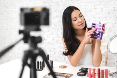 Neşeli, güzel bir kadının gülümsemesi taze, sağlıklı beyaz ten blogcusu kameranın önünde kendini videoya kaydediyor evdeki internet sosyal ağı için makyaj malzemesi ile konuşuyor.