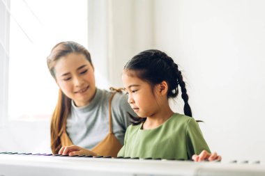 Mutlu aşk portresi Asyalı anne ve küçük Asyalı kız çocuk gülümseyip eğleniyorlar ve evde piyano dersi veriyorlar.