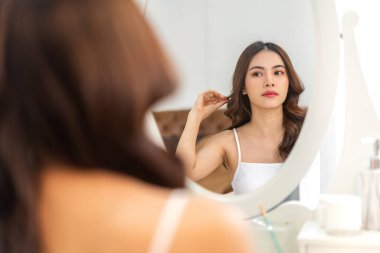 Gülümseyen, güzel, güzel Asyalı kadın güzellik bembeyaz giysiler içinde temiz, sağlıklı beyaz ten. Düşen ve eğlenen kız Home.Asia güzellik salonundaki aynaya bak.