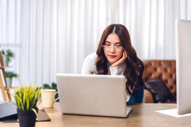 Genç gülümseyen mutlu Asyalı kadın evdeki odada dizüstü bilgisayar kullanarak rahatlıyor. Ev konseptinden çalışıp klavyede yazan genç yaratıcı kız.