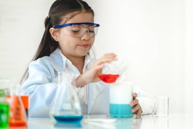 Tatlı küçük kız öğrenci araştırma öğreniyor ve kimyasal bir deney yapıyor aynı zamanda fen bilimleri sınıfında sıvıyı analiz edip karıştırıyor. Eğitim ve bilim konsepti.