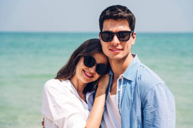 Romantik aşıklar. Genç mutlu çift, tropikal sahilde sarılıp kumsalda durup eğleniyor ve dinleniyorlar.