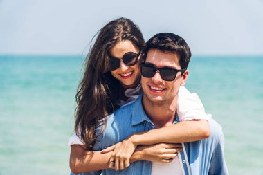 Romantik aşıklar. Genç mutlu çift, tropikal sahilde sarılıp kumsalda durup eğleniyor ve dinleniyorlar.