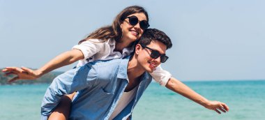 Romantik aşıklar. Genç mutlu çift, tropikal sahilde sarılıp kumsalda durup eğleniyor ve dinleniyorlar.