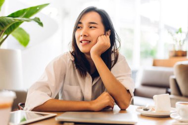 Gülümseyen mutlu Asyalı bir kadının portresi dizüstü bilgisayar teknolojisini kullanarak rahatlıyor. Genç hippi Asyalı kız serbest çalışıyor ve kafeteryada yeni fikirler üretiyor.