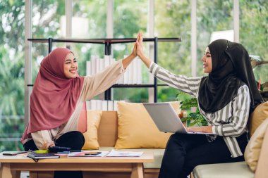 Genç, gülümseyen, mutlu, Asyalı Müslüman bir kadın dizüstü bilgisayarını kullanarak rahatlıyor ve evde video konferansı yapıyor. Ev konseptinden çalışma.