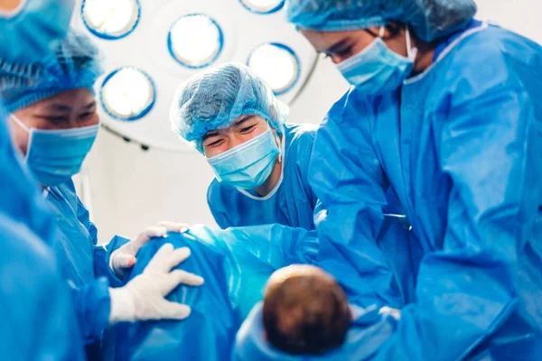 Professional anesthesiologist doctor medical team and assistant is performing baby cesarean section and hold the newborn baby giving birth with surgery equipment in modern hospital operation room