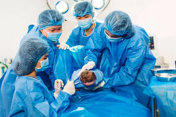 Professional anesthesiologist doctor medical team and assistant is performing baby cesarean section and hold the newborn baby giving birth with surgery equipment in modern hospital operation room