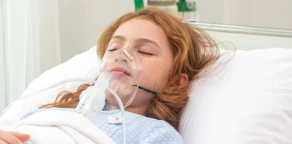 Cute little asian girl with oxygen pipe and using oxygen mask for inhalations and treatment on her face on bed in the hospital.health care,support concept