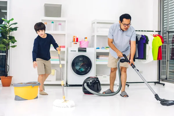 家庭で掃除をしたり 掃除機でほこりを拭いたりしながら家で一緒に掃除をしたりする家庭的な家事を楽しんでいるアジアの子供の男の子の息子を教える父 — ストック写真