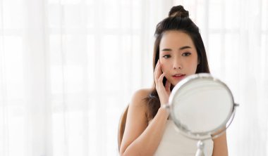 Gülümseyen, güzel, güzel Asyalı kadın güzellik bembeyaz giysiler içinde temiz, sağlıklı beyaz ten. Düşen ve eğlenen kız Home.Asia güzellik salonundaki aynaya bak.