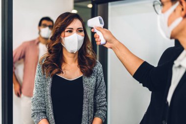 Bir grup profesyonel Asya işi ve ofiste koruyucu maske takarak koronavirüs için karantinada çalışmadan önce vücut ısısını ölçmek için kızılötesi termometre kullanılıyor.