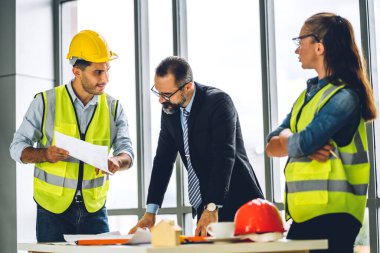 İnşaat sahasında planlar ve inşaat araçlarıyla çalışan miğferli ekip mühendisi ustabaşı.