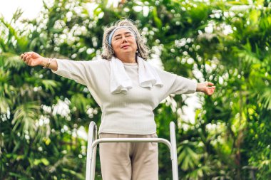 Yaşlı, mutlu Asya 'lı kadınların portresi ayakta gülümseyen, kollarını uzatan ve doğa ile eğlenen yeşil parktaki temiz havayı hisseden.