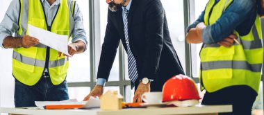 İnşaat sahasında planlar ve inşaat araçlarıyla çalışan miğferli ekip mühendisi ustabaşı.