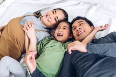 Portrenin en üst görüntüsü mutlu bir şekilde gülümseyen Asyalı bir aile babası ve annesi ve genç bir ebeveyni olan küçük Asyalı bir kız kameraya bakıyor.