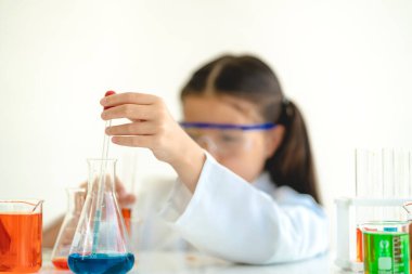 Tatlı küçük kız öğrenci araştırma öğreniyor ve kimyasal bir deney yapıyor aynı zamanda fen bilimleri sınıfında sıvıyı analiz edip karıştırıyor. Eğitim ve bilim konsepti.