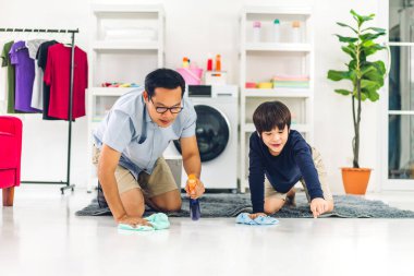 Babası Asyalı çocuğa dezenfekte spreyi kullanmasını ve evde birlikte temizlik yaparken yerleri paçavralarla silmesini öğretiyor.