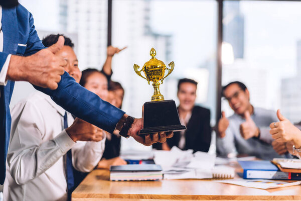 Превосходная группа случайных деловых людей, расслабляющихся и держащих в руках золотой трофей, добивающихся успеха.