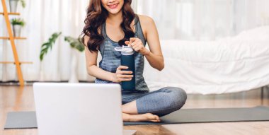 Spor kıyafetli, spor elbiseli, ince Asyalı, portre sporu. Rahatlayıp, bir şişeden su içen, yatak odasında dizüstü bilgisayarla spor yapan bir kadın. Diet. Spor ve sağlıklı yaşam tarzı.