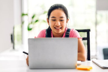 Okul çocuğu küçük kız öğreniyor ve dizüstü bilgisayara bakıyor ev ödevi yapıyor çevrimiçi eğitim sistemi ile bilgi öğreniyor. Evde öğretmenle çocuk video konferansı