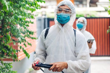 Koruyucu maske takan dezenfekte işçileri ve müşteri evindeki Coronavirüs 'ü öldürmek için beyaz takım elbise dezenfektan sprey temizlik virüsü kullanan profesyonel ekipler.