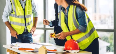 İnşaat sahasında planlar ve inşaat araçlarıyla çalışan miğferli ekip mühendisi ustabaşı.