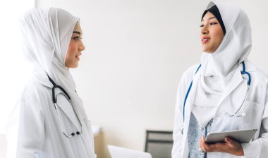 Hastane masasında pano ve tablet bilgisayarla çalışan iki Asyalı Müslüman kadın doktor. Sağlık ve ilaç servisi.