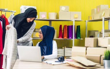 Müslüman, iki Asyalı serbest çalışan kadın internetten alışveriş yapıyor ve karton kutuları evde, iş yeri online nakliye ve teslimat konseptiyle kontrol listesi düzenliyor.