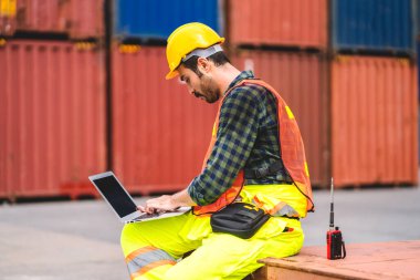 Kasklı profesyonel mühendis konteynır ustabaşı ayakta çalışıyor ve telsiz kullanıyor. Stokları yükleme için konteynıra koyuyor. Lojistik ulaşım ve iş sektörü ihracatı