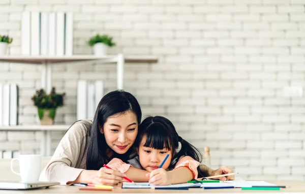 ポートレート愛アジアの家族の母親と小さなアジアの女の子学習と書き込みで本とともに鉛筆作り宿題で自宅 — ストック写真