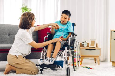 Asyalı fizyoterapistin portresi engelli çocuk sağlığı sorununa rehabilitasyon kliniğinde tekerlekli sandalyede oturarak yardım ve oyun oynayarak yardımcı oluyor.