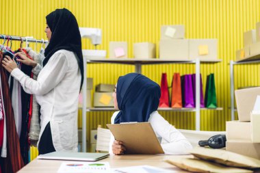 Müslüman, iki Asyalı serbest çalışan kadın internetten alışveriş yapıyor ve karton kutuları evde, iş yeri online nakliye ve teslimat konseptiyle kontrol listesi düzenliyor.