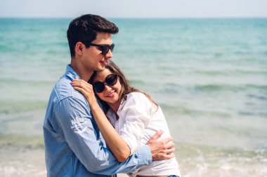 Romantik aşıklar. Genç mutlu çift, tropikal sahilde sarılıp kumsalda durup eğleniyor ve dinleniyorlar.