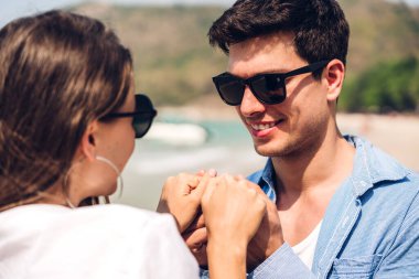 Romantik aşıklar. Genç mutlu çift, tropikal sahilde sarılıp kumsalda durup eğleniyor ve dinleniyorlar.