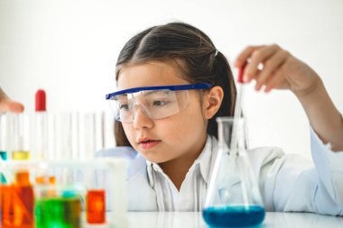 Tatlı küçük kız öğrenci araştırma öğreniyor ve kimyasal bir deney yapıyor aynı zamanda fen bilimleri sınıfında sıvıyı analiz edip karıştırıyor. Eğitim ve bilim konsepti.