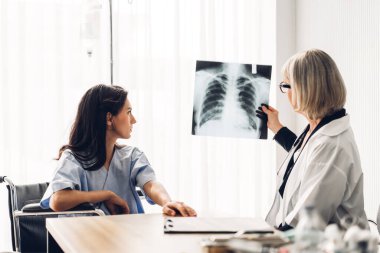 Steteskoplu üniforma giyen kıdemli kadın doktor, akciğer zatürresi olan hastanın göğüs röntgeni görüntülerini tarayıp incelemeye yardımcı oluyor.