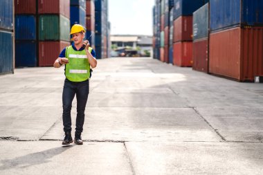 Kasklı profesyonel mühendis konteynır ustabaşı ayakta çalışıyor ve telsiz kullanıyor. Stokları yükleme için konteynıra koyuyor. Lojistik ulaşım ve iş sektörü ihracatı