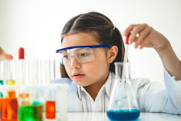 Cute little girl student child learning research and doing a chemical experiment while making analyzing and mixing liquid in glass at science class in school.Education and science concept