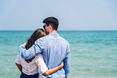 Romantik aşıklar. Genç mutlu çift, tropikal sahilde sarılıp kumsalda durup eğleniyor ve dinleniyorlar.