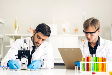 Profesyonel iki bilim adamı test tüpünde sıvı analiz ederken ve karıştırırken kimyasal bir deney yapıyor. Genç bilim adamı laboratuvarda cam üzerine kimyasal örnekler bırakıyor.