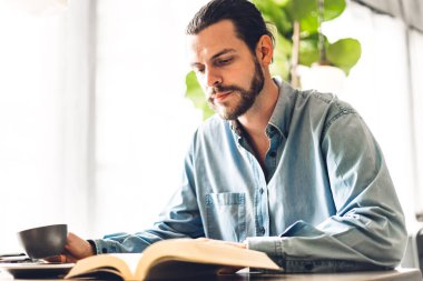 Yakışıklı hippi kahve içiyor, gazete okuyor, kitap okuyor ve kafe ve restoranda sandalye üzerinde otururken magazin dergilerine bakıyor.