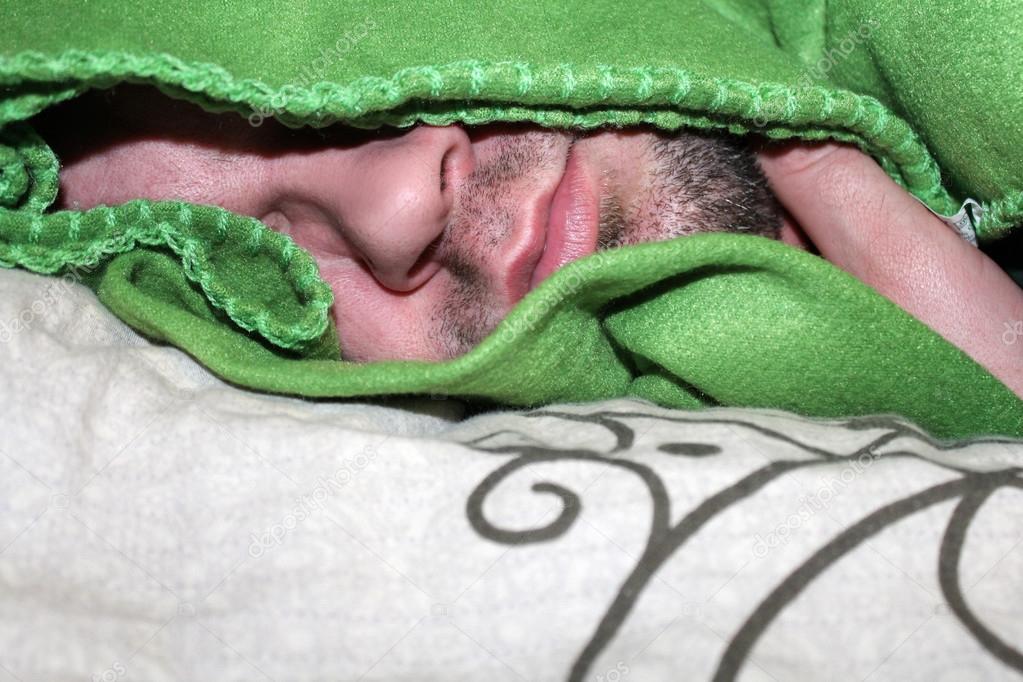 Sleeping man covered with a green blanket.