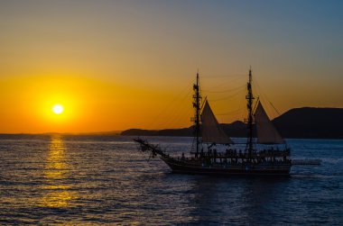 Batan güneşin arka plan üzerinde iki direkli yelkenli gemi.