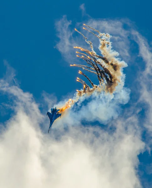 Military aircraft fighter SU-27 nose-dive, performs the maneuver with the ejection of heat missiles, releasing a plume of hot gases. — Stock Photo, Image