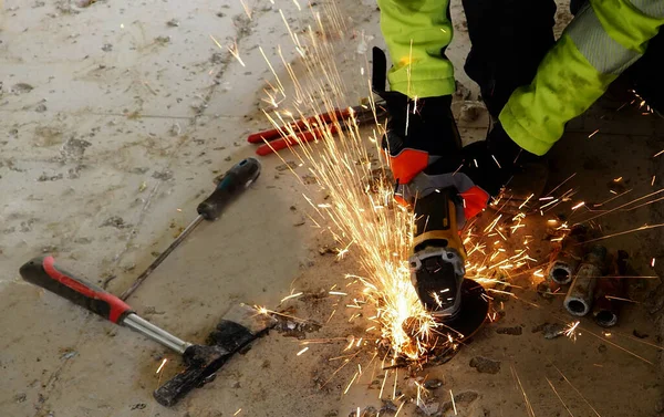 shows or displays a person working in the construction industry, construction industry work, work clothes and gloves, work tools, angle grinder, sparks from cutting iron, concrete, view from above,