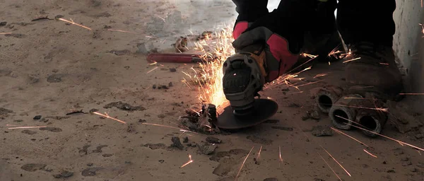shows or displays a person working in the construction industry, construction industry work, work clothes and gloves, work tools, angle grinder, sparks from cutting iron, concrete