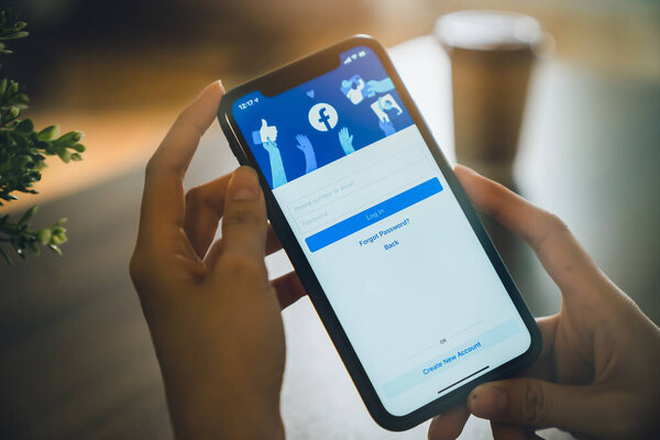 BANGKOK, THAILAND - October 31, 2020 : Hand is holding smartphone and the Facebook screen on apple IPhone, Social media are using for information sharing and networking.